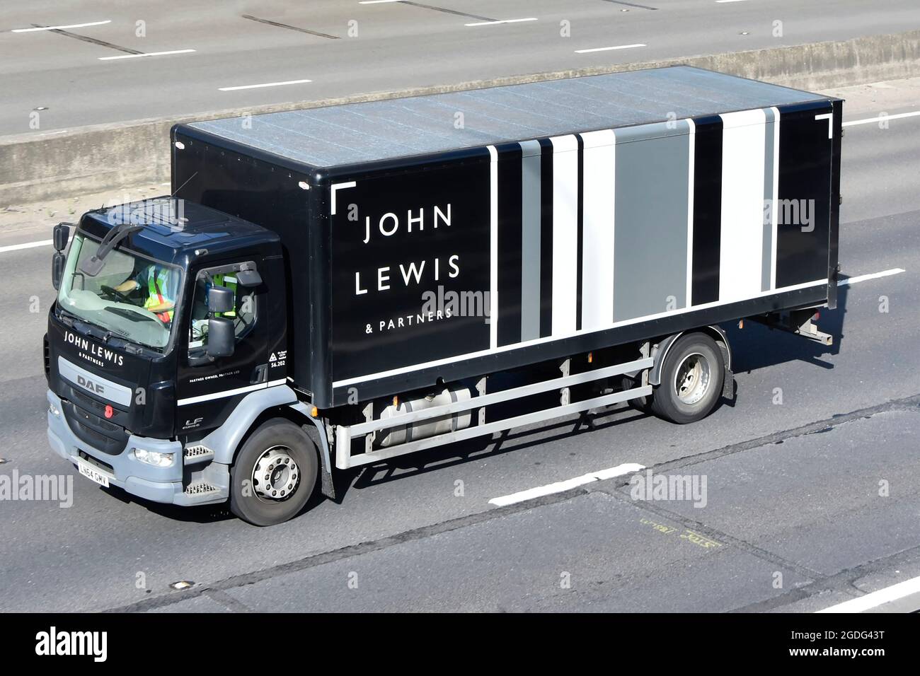 Vista frontale e dall'alto di John Lewis & Partners Retail Consumer Business Transport Delivery camion e cabina con conducente che viaggia lungo l'autostrada del Regno Unito Foto Stock