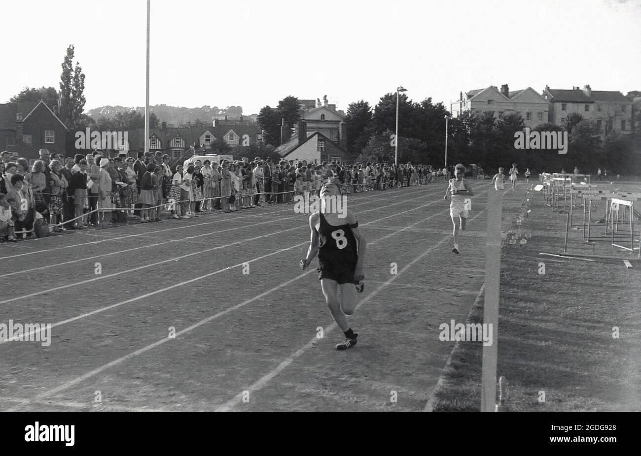 1964, storico, fuori in una giornata sportiva delle scuole della contea e guardato da spettatori di genitori e famiglia, un ragazzo adolescente che corre su una pista di cenere facendo uno sforzo enorme per terminare la corsa al primo posto, Exeter, Devon, Inghilterra, Regno Unito. Foto Stock