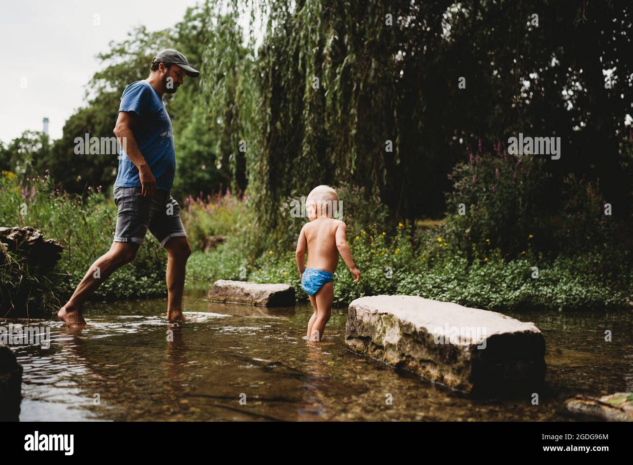 Padre e figlio che camminano in acqua in torrente in estate Foto Stock