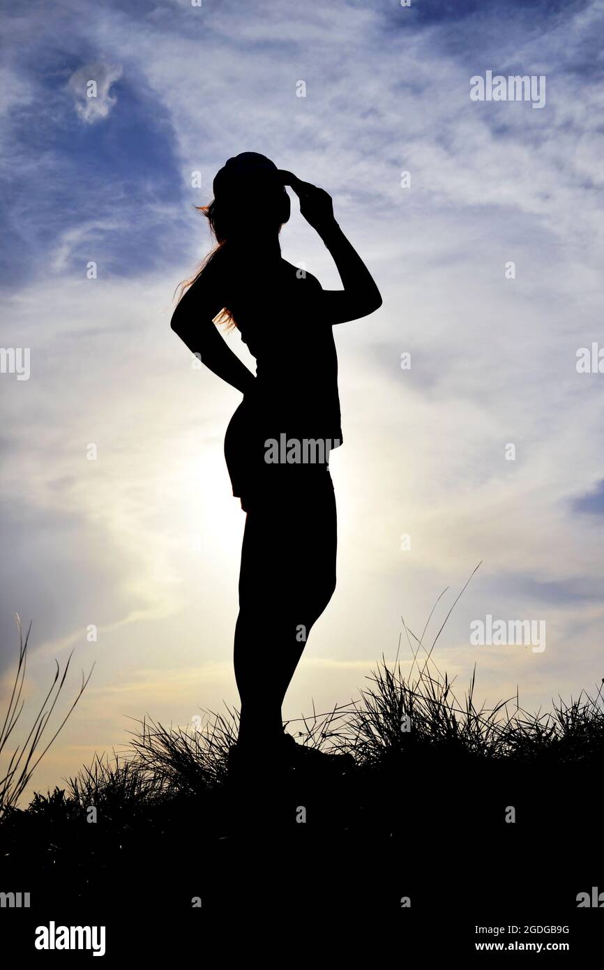 Silhouette di un atleta che si alza in piena crescita e tiene un cappello. Foto Stock