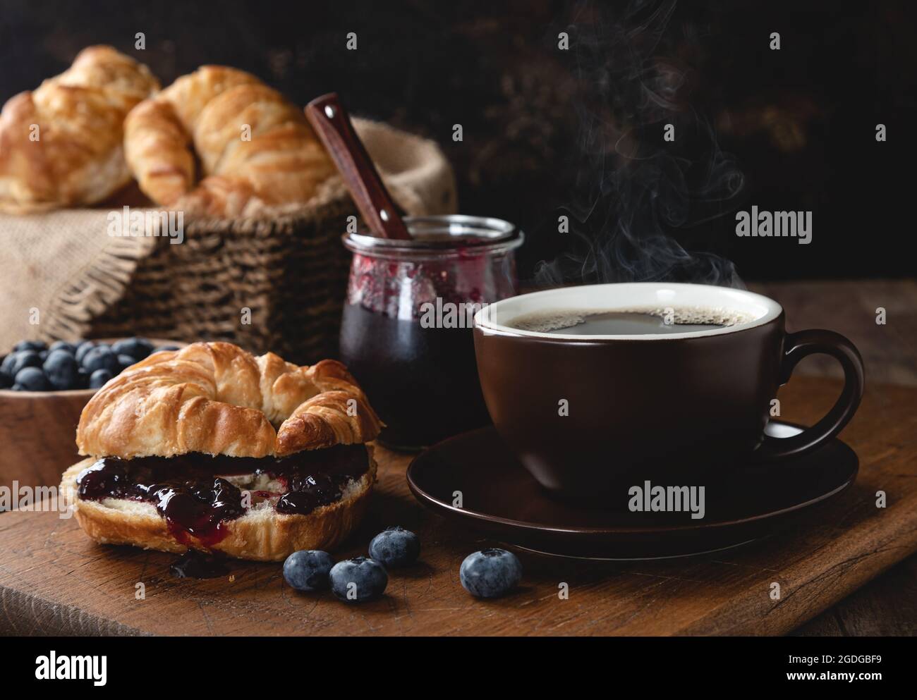 Croissant con marmellata di mirtilli e tazza di caffè caldo e mirtilli freschi su un tavolo di legno Foto Stock