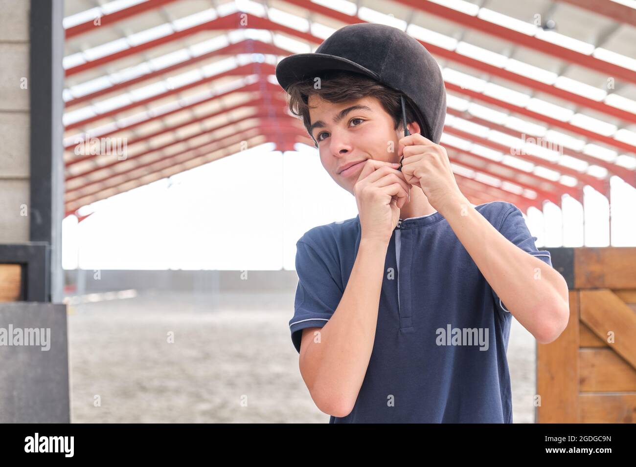 Ragazzo adolescente che mette un casco da cavalcare sulla testa. Foto Stock