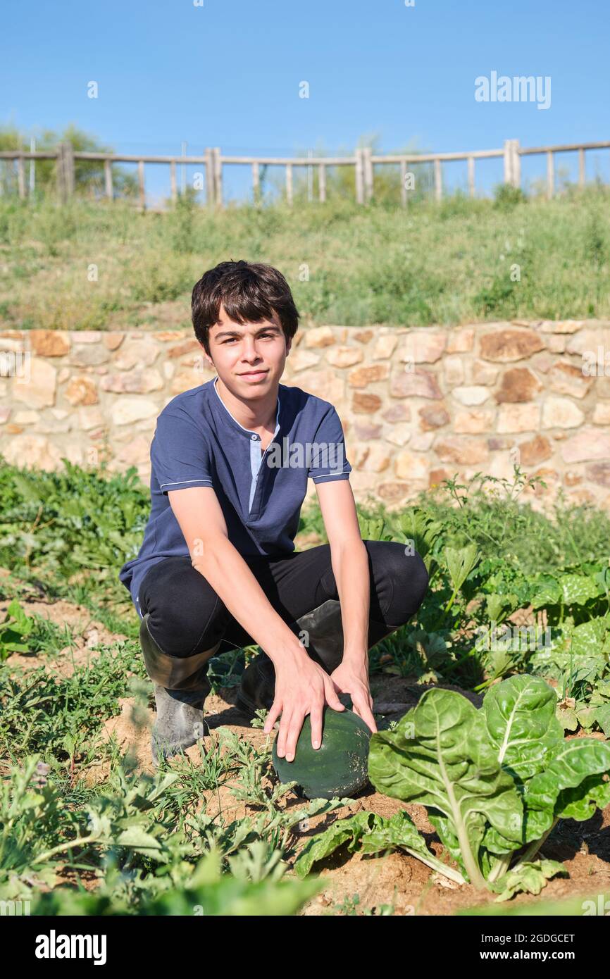 Giovane agricoltore in un campo con frutta e pianta di anguria guardando la macchina fotografica. Foto Stock