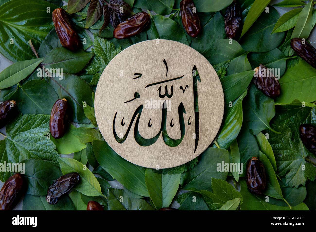Nome di Allah in arabo su legno d'oro, foglie verdi e datteri di sfondo frutta. Calligraphy significa il Dio al Mighty della religione islamica. Foto Stock