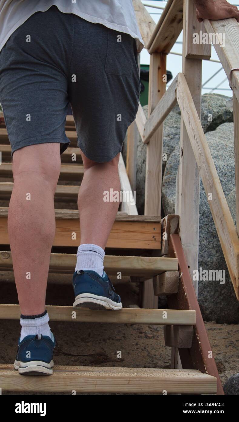vista da dietro dei piedi di un uomo che sale su una scala in legno sulla spiaggia Foto Stock