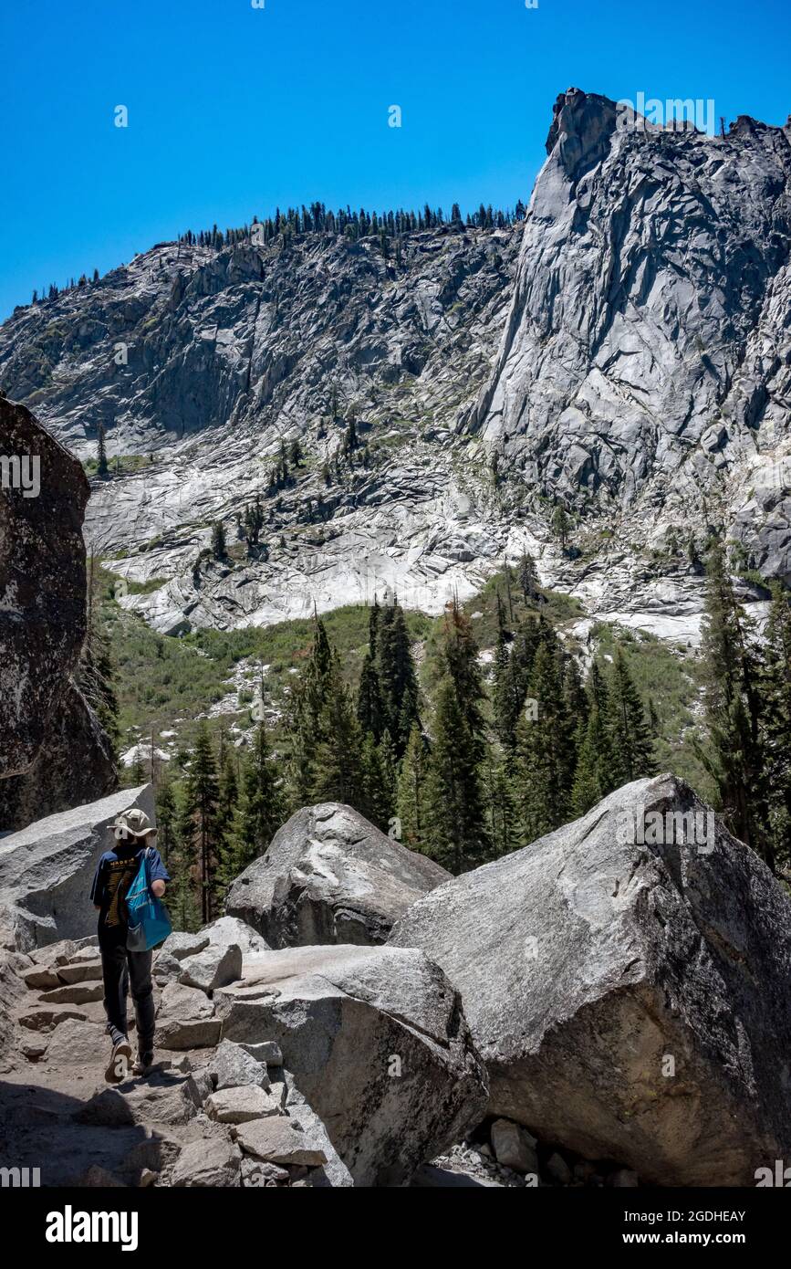 Un giovane escursionista segue il Tokopah Falls Trail passando accanto a massi di granito con una vista mozzafiato sulla Tokopah Valley e la cupola di granito della torre di guardia. Foto Stock