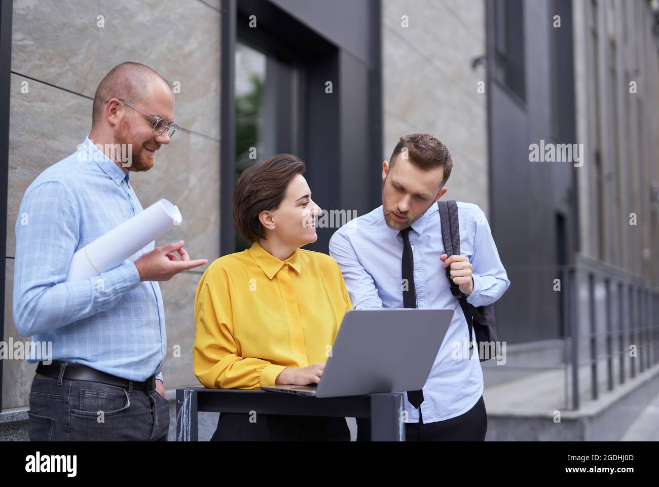 I progettisti o il team di architetti che guardano il progetto e il notebook come presentazioni all'aperto. Uomini d'affari, uomini e donne in abiti casual in piedi fuori, progetto di brainstorming Foto Stock