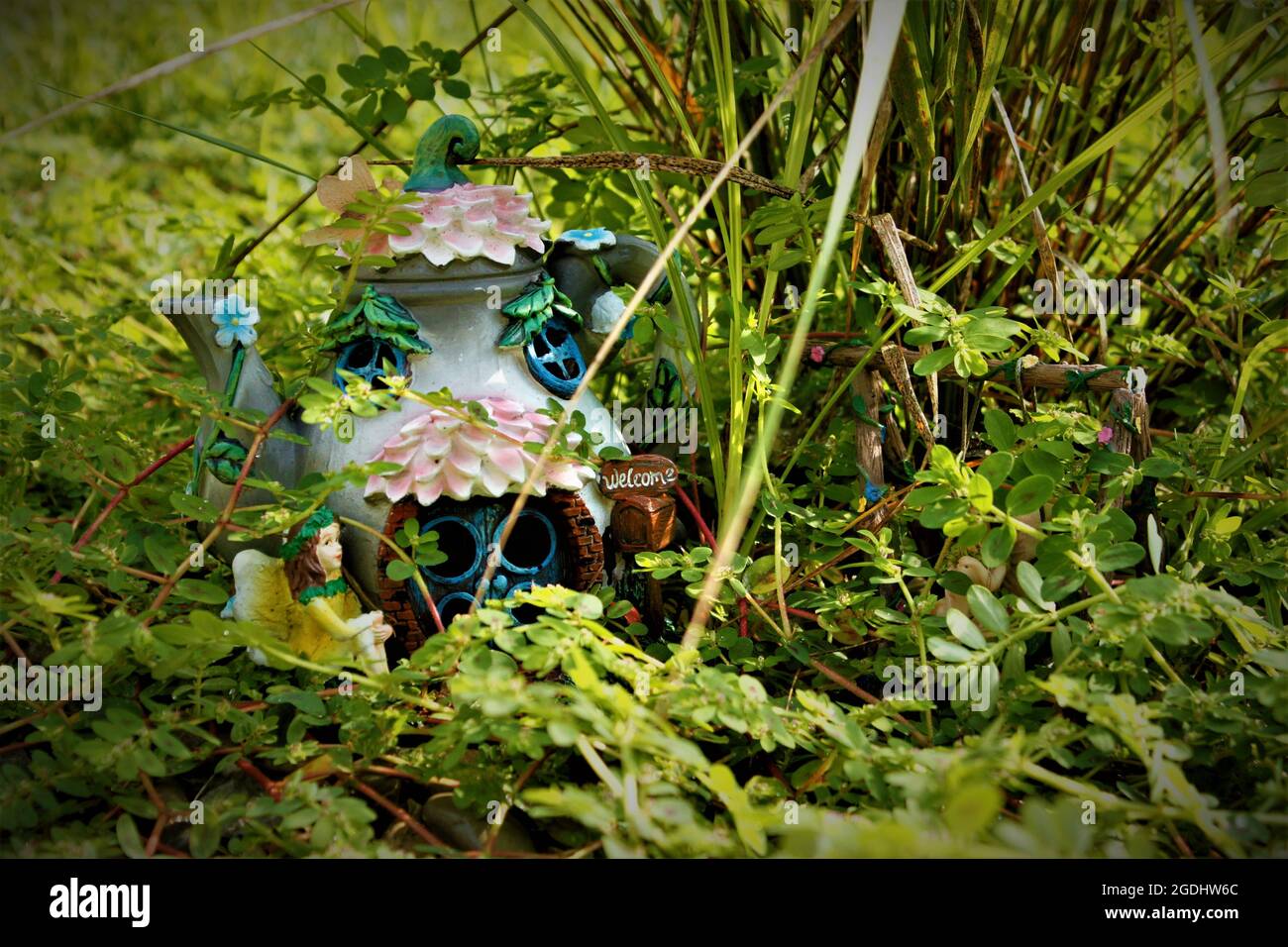 Tea Pot Fairy House con un cartello di benvenuto in un giardino naturale di roccia adornato da spurge macchiato Foto Stock