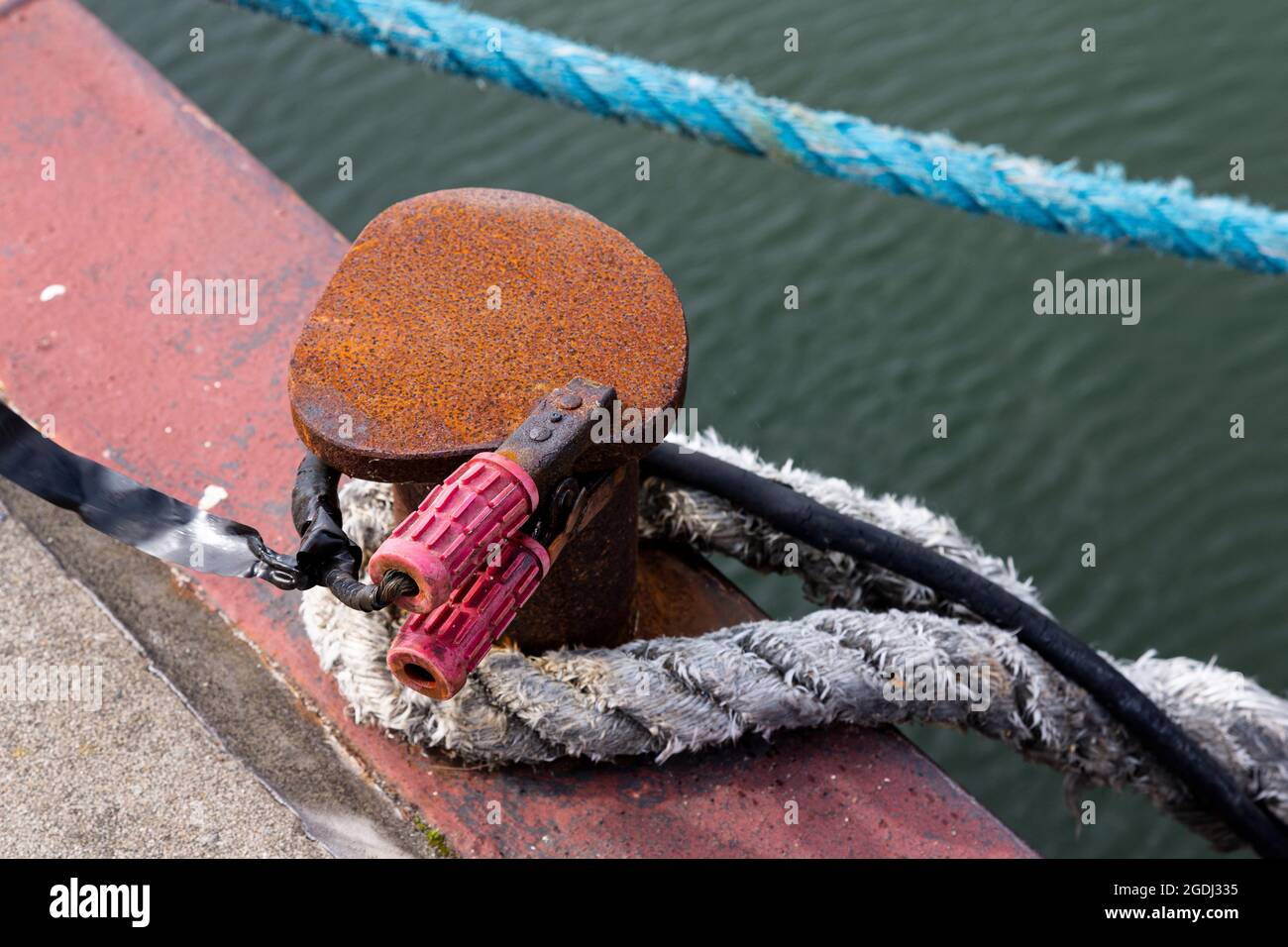 Una corda e un cavo elettrico con morsetti su un paletto nel porto. Foto Stock
