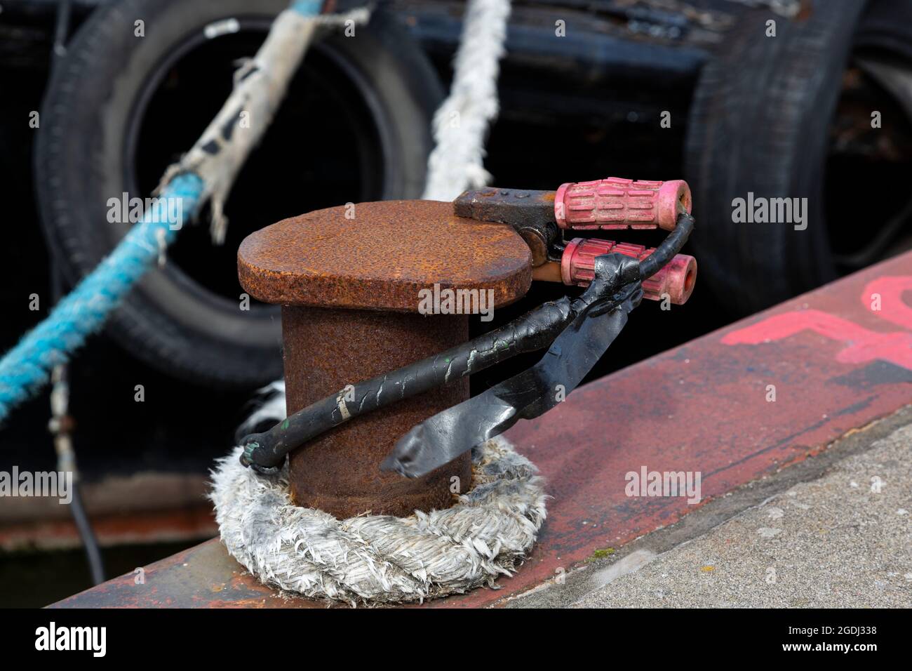 Una corda e un cavo elettrico con morsetti su un paletto nel porto. Foto Stock