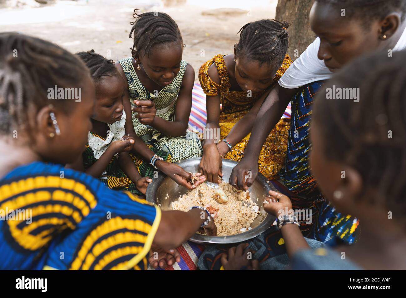 Gruppo di ragazze africane che si siedono intorno ad un piatto grande con riso e verdure, godendo il loro pasto Foto Stock