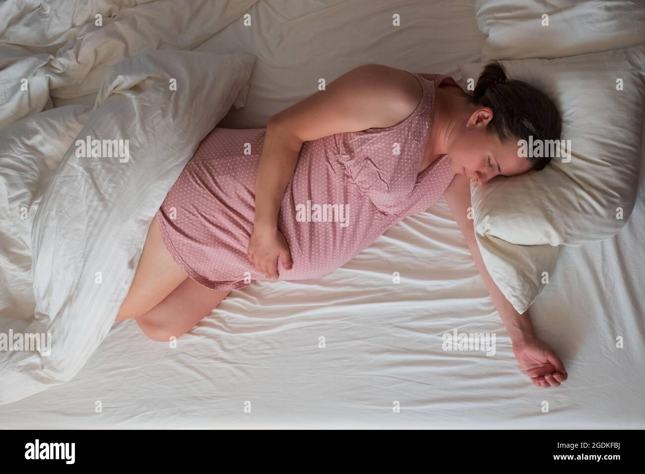 Donna caucasica incinta che dorme in abiti rosa a letto Foto Stock