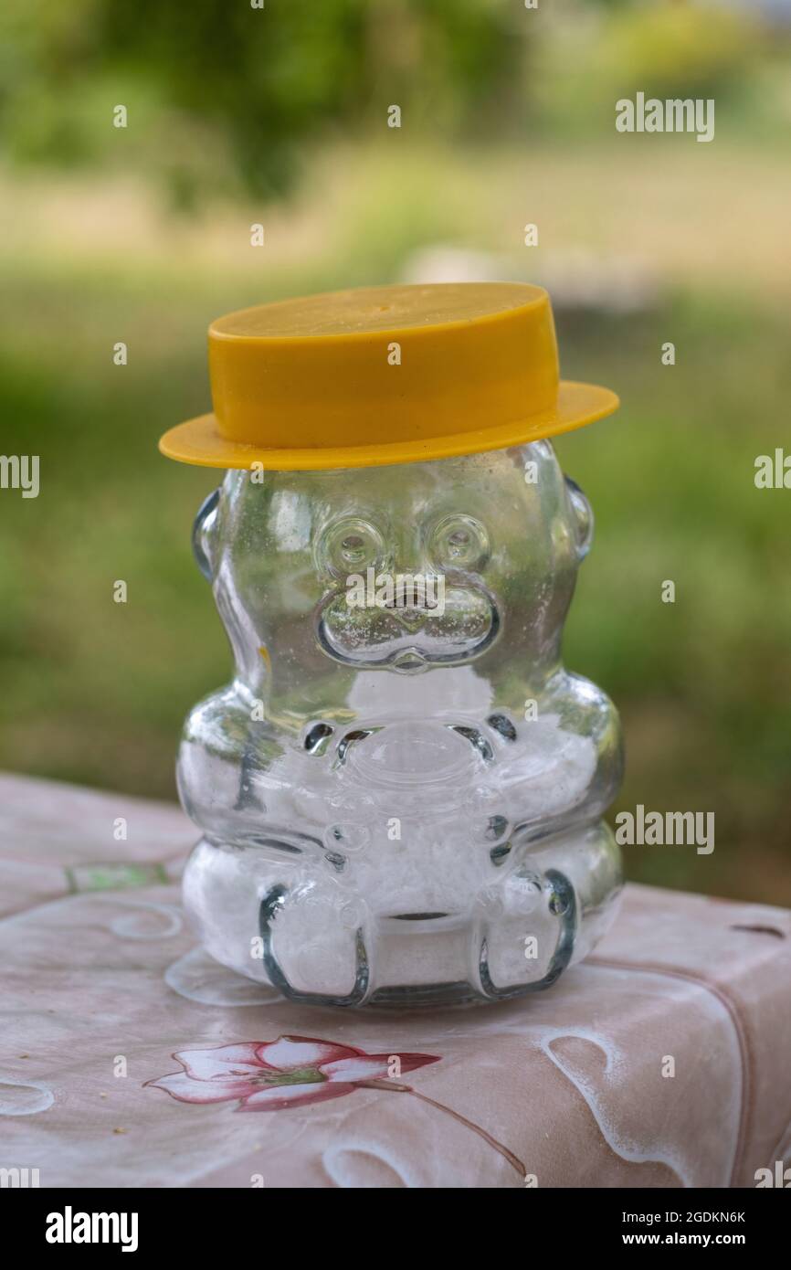 Un agitatore di sale di vetro a forma di orso in un cappello giallo, in piedi sul bordo del tavolo su uno sfondo sfocato. Foto Stock