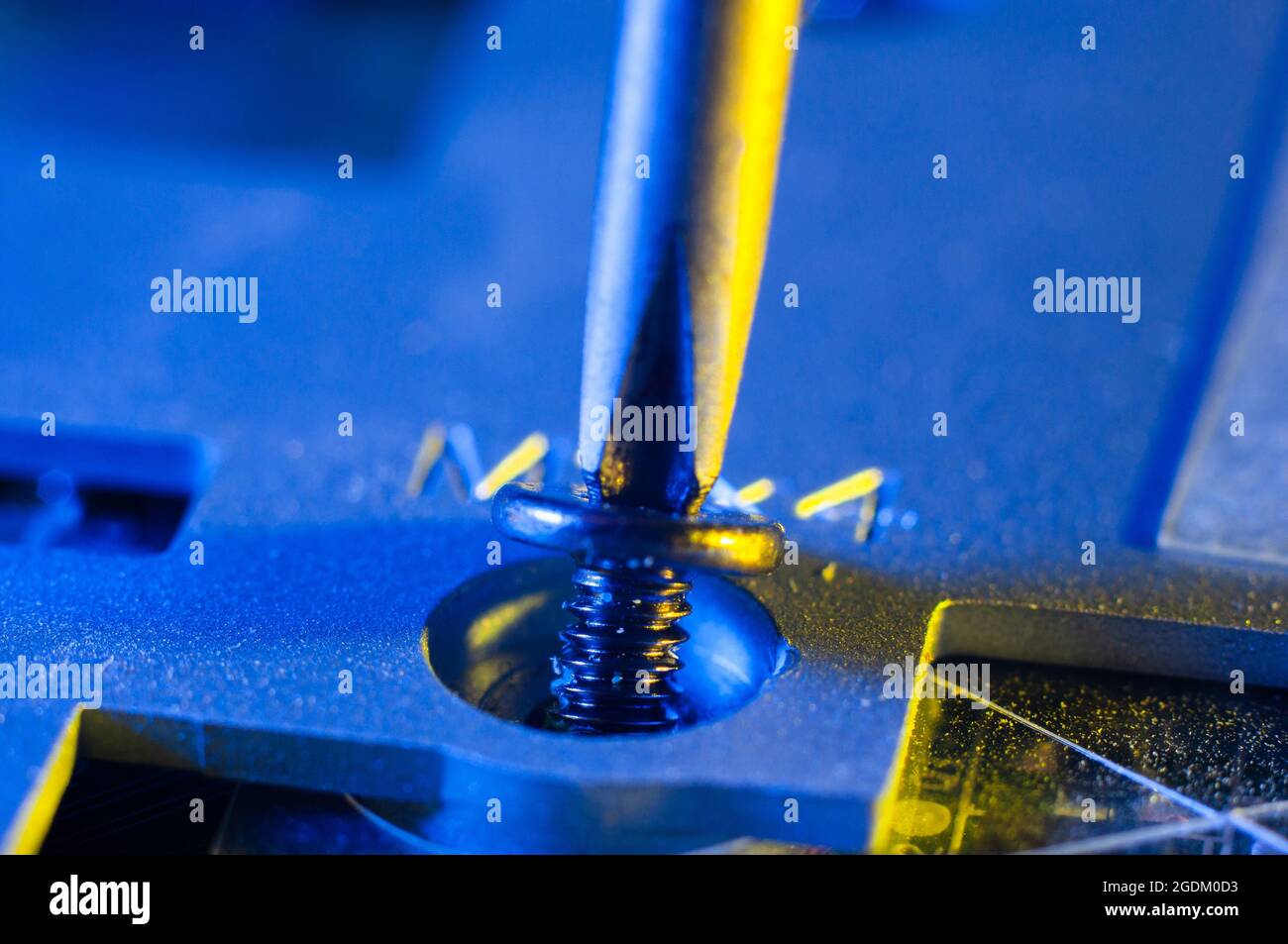 Svitando una piccola vite con un cacciavite Phillips in primo piano dalla custodia di un computer portatile, illuminazione giallo-blu Foto Stock