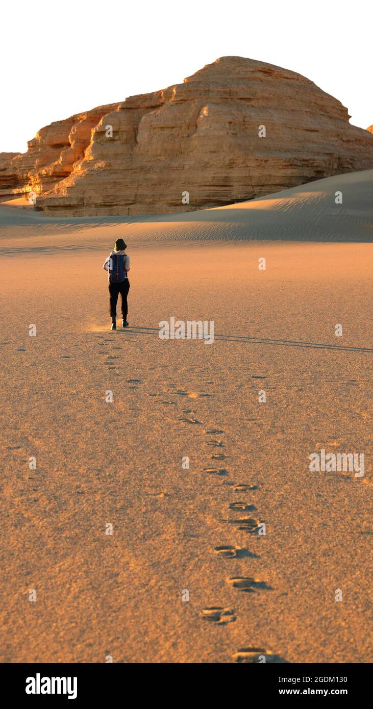 donna asiatica saccopelatrice turistica che cammina nel deserto lasciando dietro una serie di impronte Foto Stock