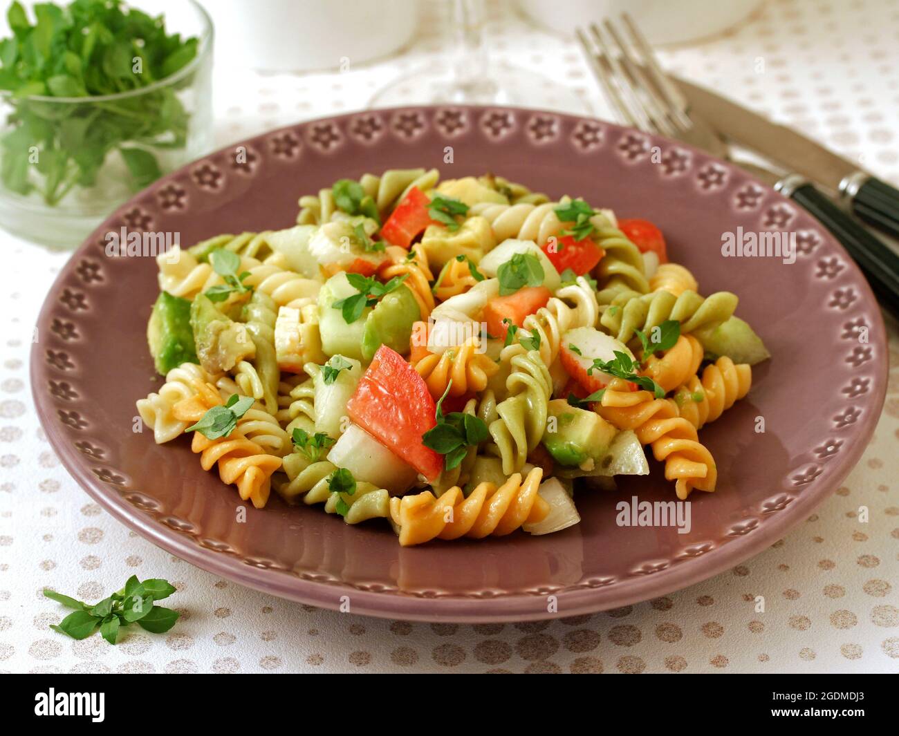 Insalata di pasta. Spirali con verdure, surimi e avocado. Con foglie di basilico come condimento. Foto Stock