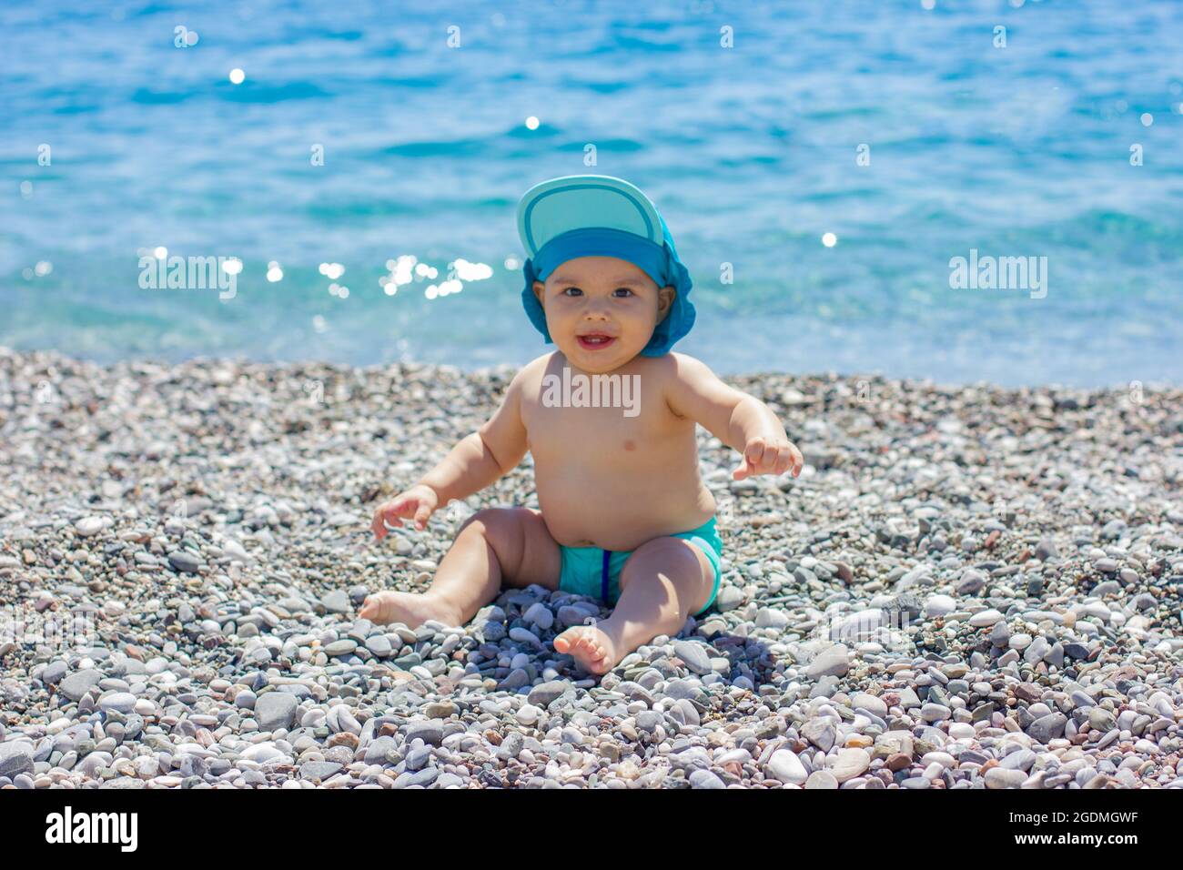 Dolce bambino chubby sulla spiaggia di ciottoli. Mare blu e sole estivo Foto Stock