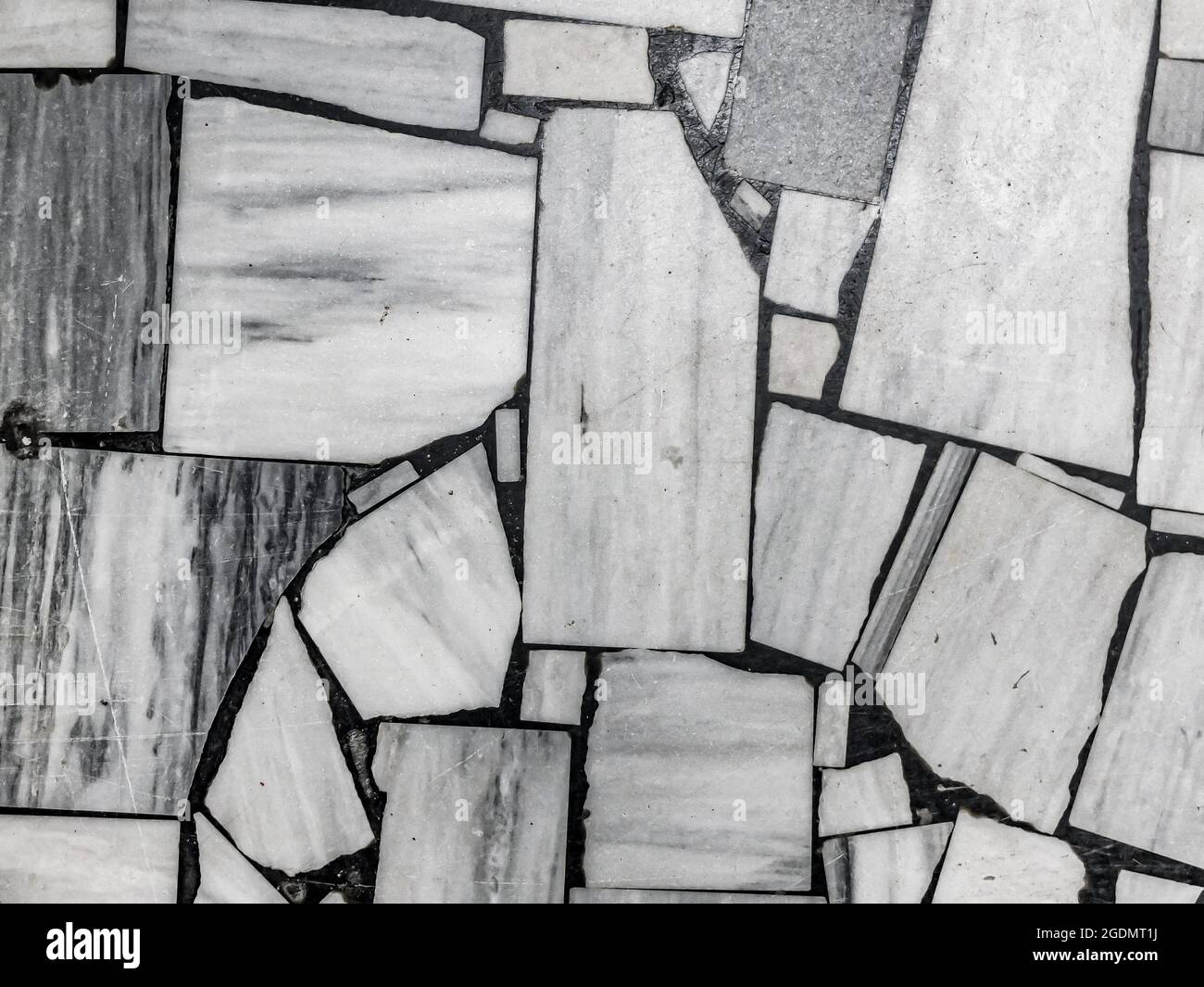 Vista dall'alto del vecchio pavimento, fatto di pezzi di varie dimensioni in marmo bianco e grigio. Sfondo a mosaico bianco e nero astratto. Foto Stock