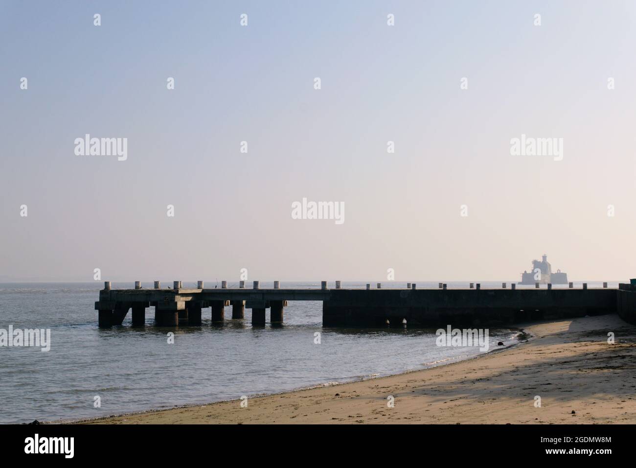 Molo di pesca porto per le barche da pesca su una spiaggia di sabbia con un faro sullo sfondo. Girato al mattino in una città costiera con luce naturale. Foto Stock