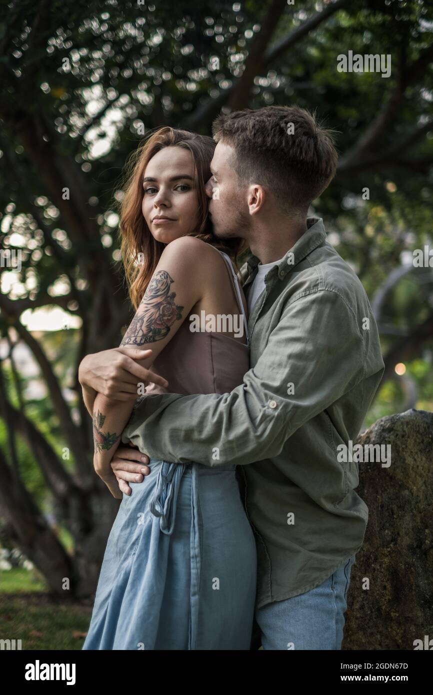 Millennial bella coppia coccolare e baciare nel parco. Guardando la fotocamera con spazio per la copia. Indossare abiti casual. Foto di alta qualità Foto Stock