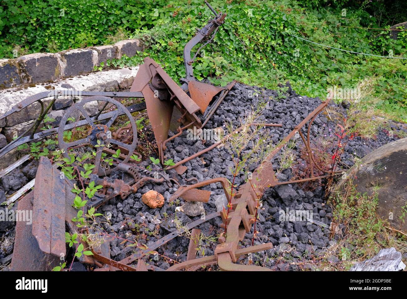 Oggetti scartati di macchinari arrugginiti giacenti in un letto di pietra e erbacce in Abbeydale Industrial Hamlet, Sheffield. Foto Stock