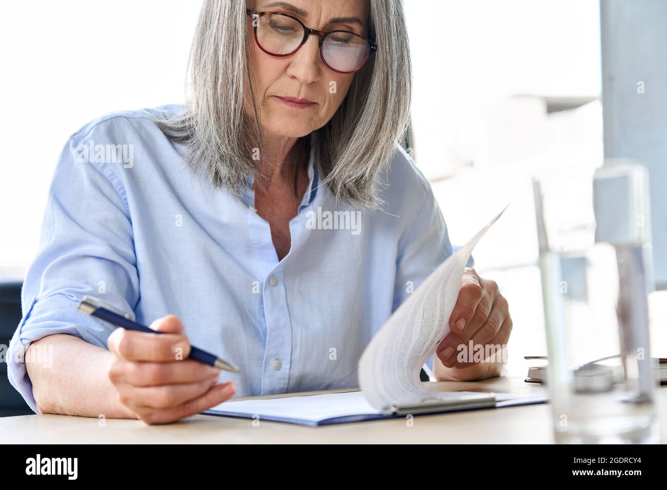 Donna d'affari più anziana focalizzata in occhiali leggendo il contratto di partnership a tavola. Foto Stock