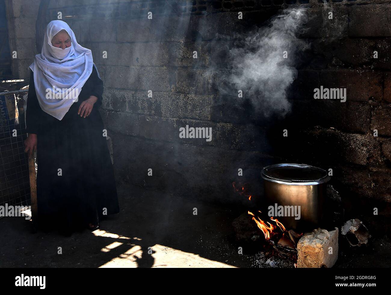 Sweida, Siria. 14 agosto 2021. Nabiha Badour, una donna siriana di 75 anni, accende la legna da ardere nel cortile della sua casa di villaggio nella campagna della provincia di Sweida, Siria meridionale, il 21 giugno 2021. Nabiha Badour si rifiuta di rimanere a casa e di aspettare che i figli si prendano cura di lei. Al contrario, sceglie di fare del duro lavoro per fare da sola la propria vita in mezzo alla dura situazione economica del paese. Credit: Ammar Safarjalani/Xinhua/Alamy Live News Foto Stock