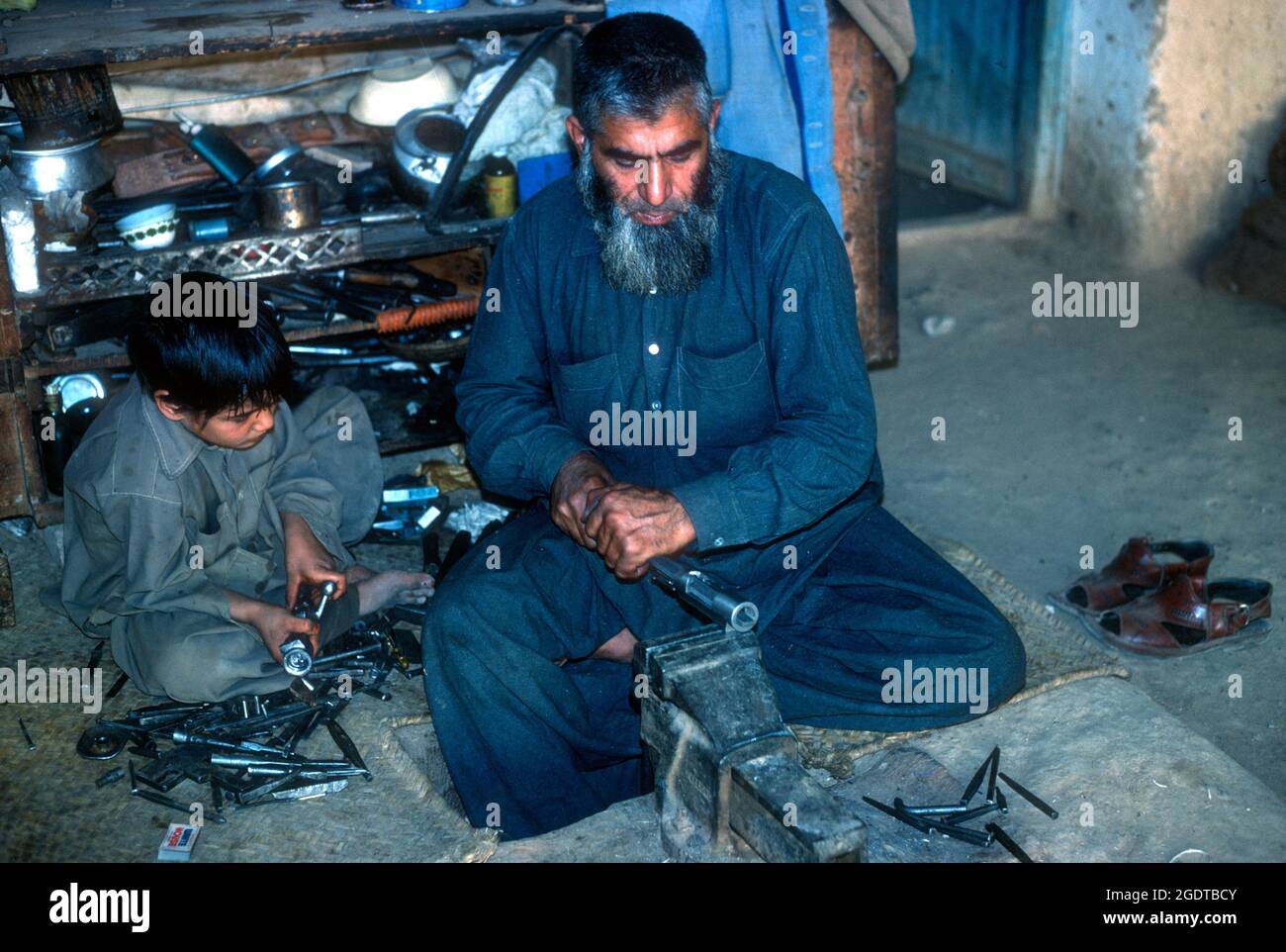 Gunsmith con figlio che fa un fucile in Dera Adam Khel. I meccanici locali possono assemblare le armi usando le parti del vecchio carrello del motore, NW Pakistan. Foto Stock