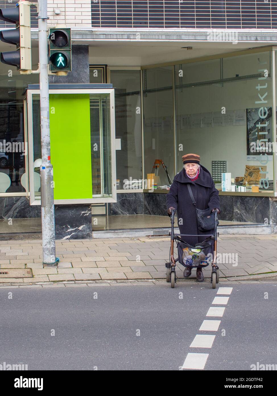 Una donna anziana attraversa solo una strada del centro, Aachen, Germania, UE. La nonna usa un camminatore con ruote per muoversi attraverso la strada. Foto Stock