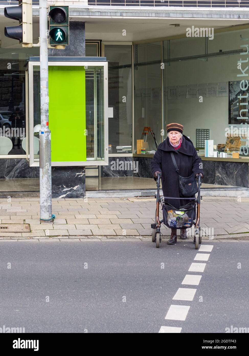 Una donna anziana attraversa solo una strada del centro, Aachen, Germania, UE. La nonna usa un camminatore con ruote per muoversi attraverso la strada. Foto Stock