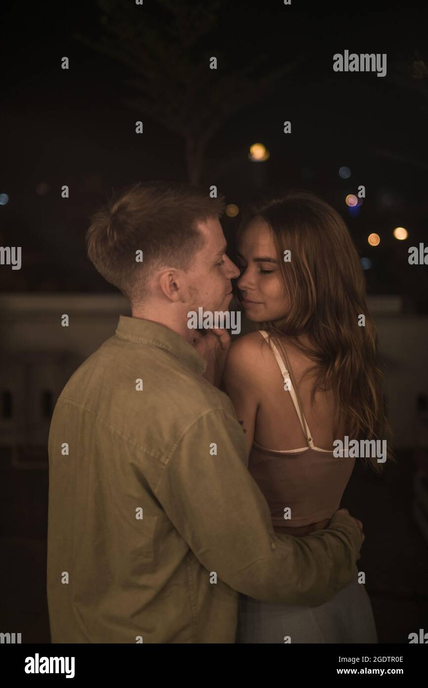 Primo piano ritratto di coppia amorevole in piedi nel buio, coccolandosi e guardando negli occhi. Coppia millenaria. Due belle persone caucasiche. Foto Stock