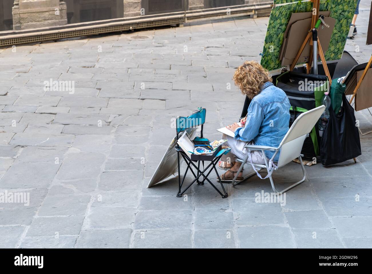 Un disegno pittore di strada si siede sulla sedia, vista posteriore. Foto Stock