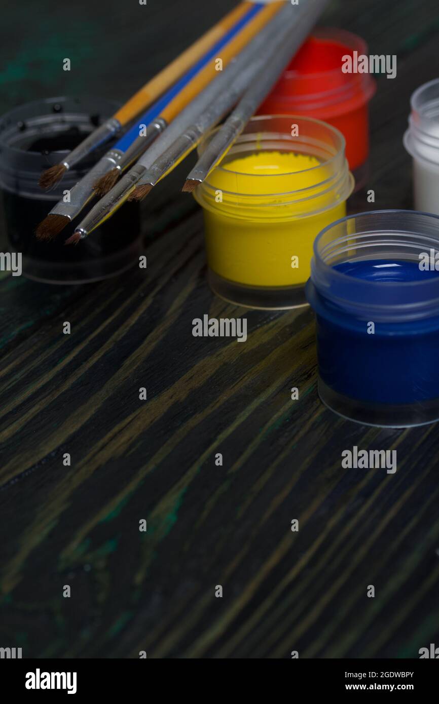 Set di gouache per la scuola. Le barattoli di vernice giacciono sulle tavole di pino. Nelle vicinanze sono presenti pennelli. Foto Stock