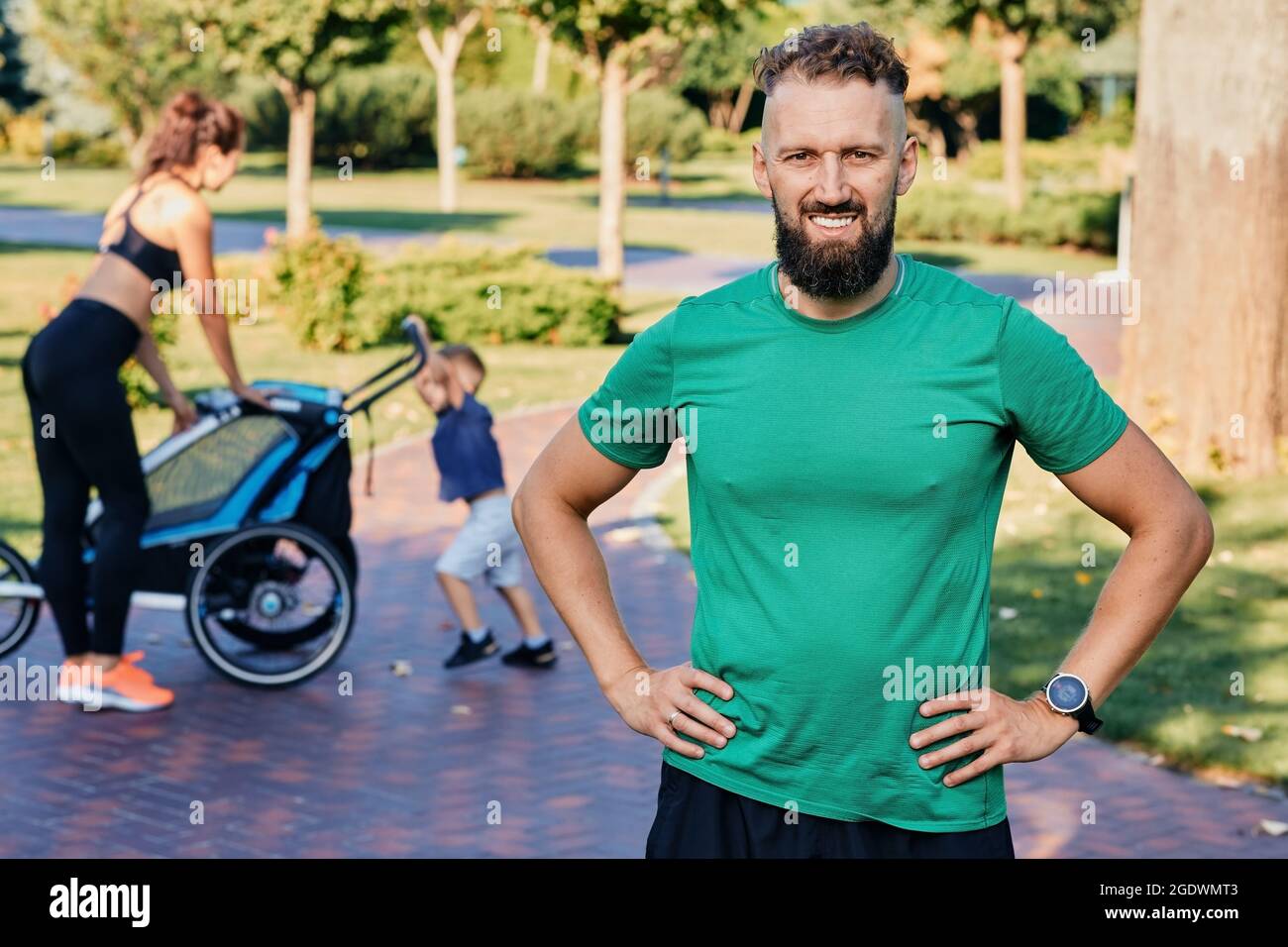 Ritratto di un padre sportivo che indossa abiti sportivi sullo sfondo di sua moglie e figlio dopo un allenamento e gli esercizi in un parco cittadino. Stile di vita sano WIT Foto Stock