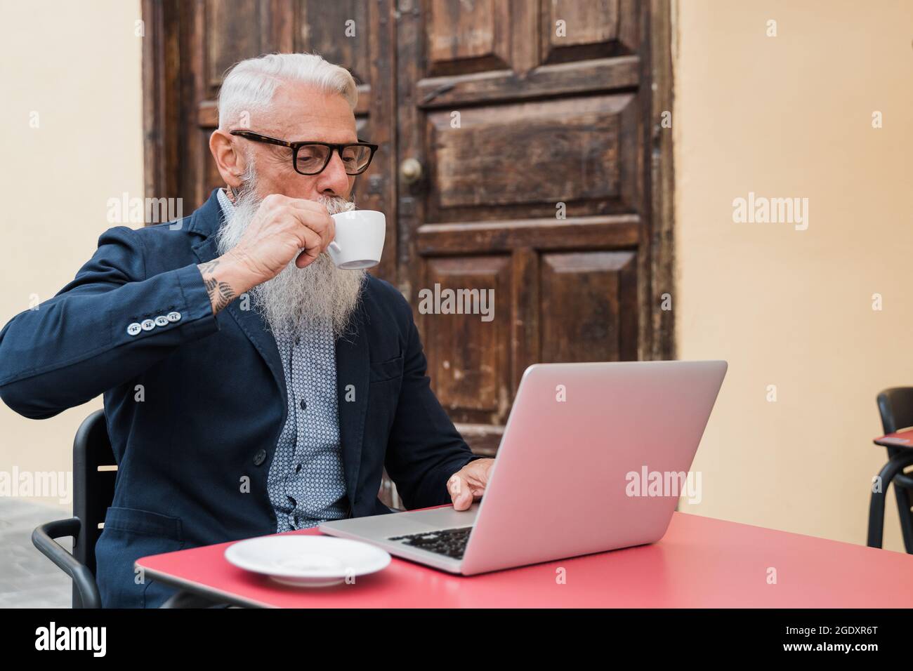 Uomo d'affari senior hipster che usa un computer portatile mentre beve caffè all'aperto al bar caffetteria - stile di vita e concetto tecnologico gioioso per anziani - Focus Foto Stock