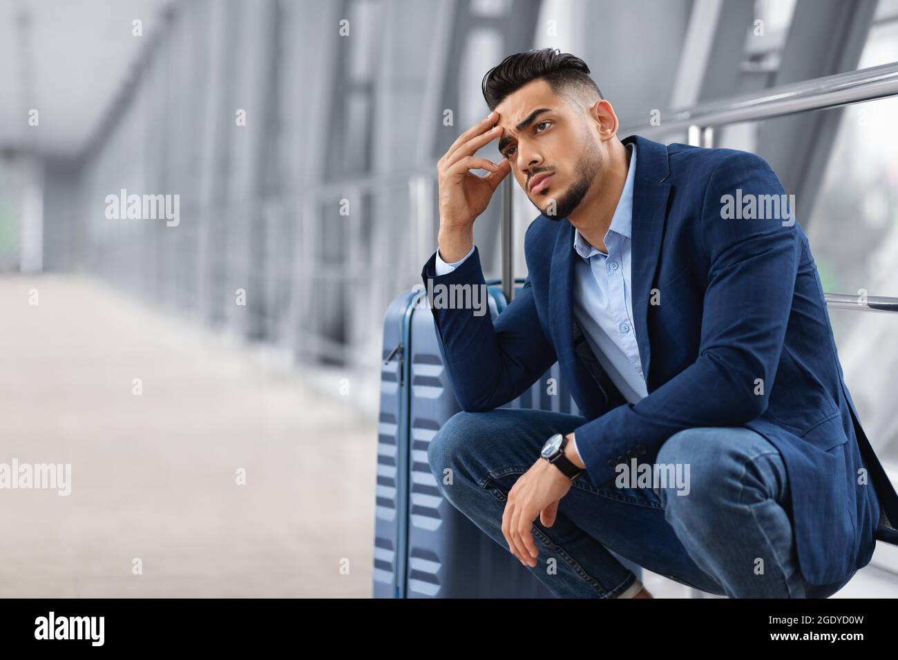 Ritardo di volo. Pensive Arab Man in attesa con i bagagli nel terminal dell'aeroporto Foto Stock
