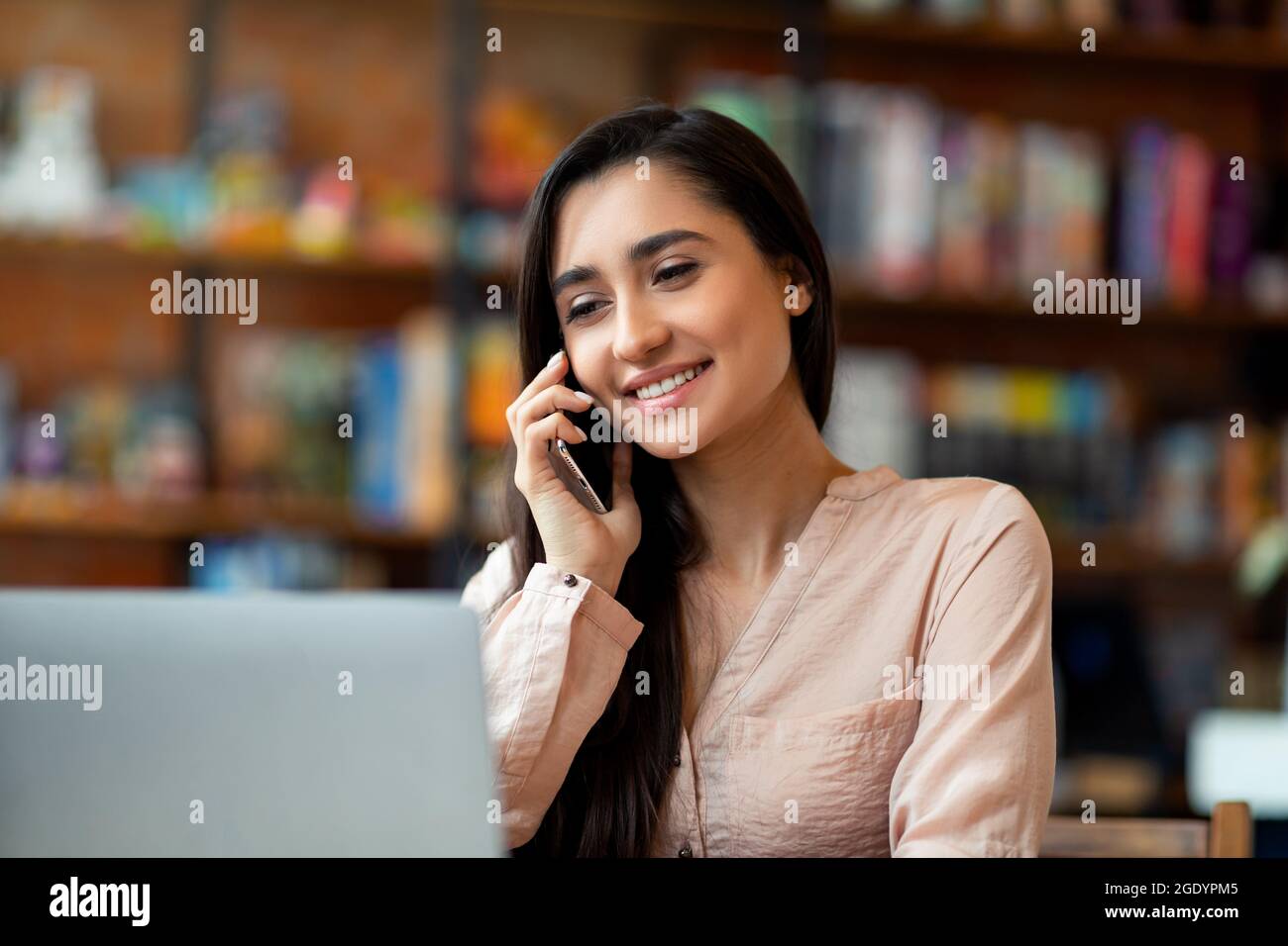 Entusiasta imprenditore latino che parla su smartphone mentre lavora su un computer portatile in un bar, spazio libero Foto Stock