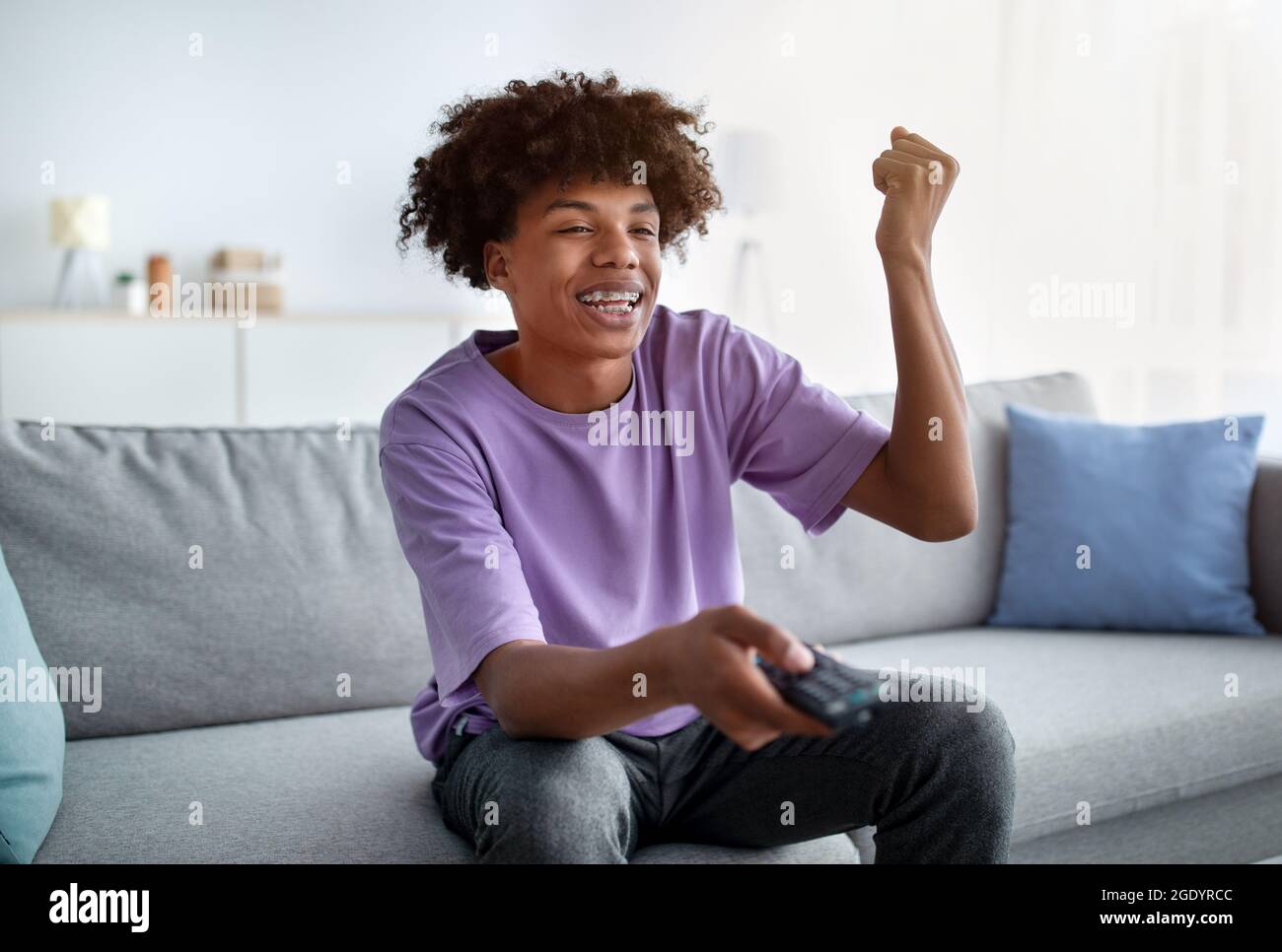 Teen afroamericano eccitato con telecomando godendo film, facendo sì gesto a casa Foto Stock