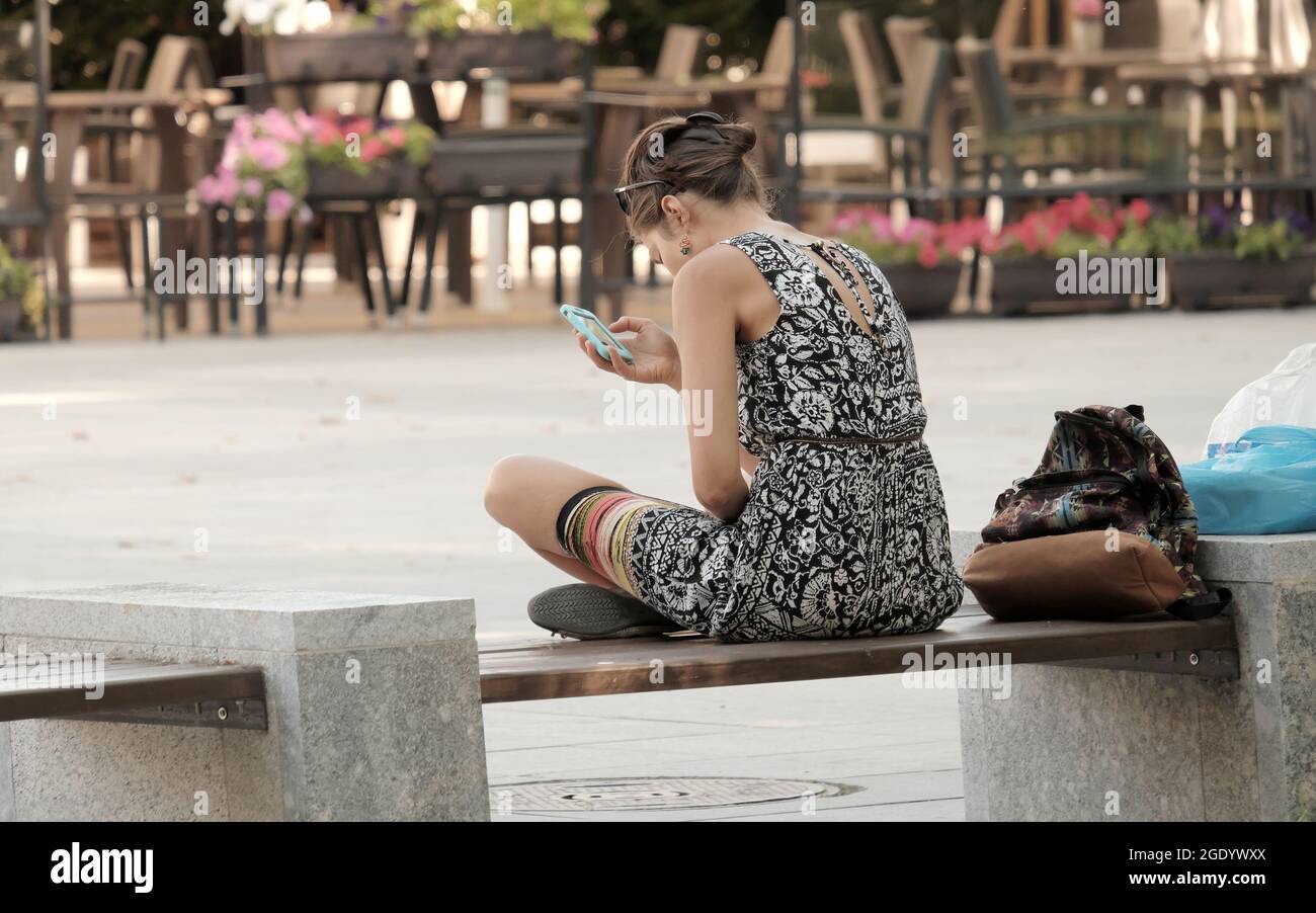 Giovane donna seduta sulla panchina e guardando il suo cellulare a Sofia, Bulgaria Foto Stock