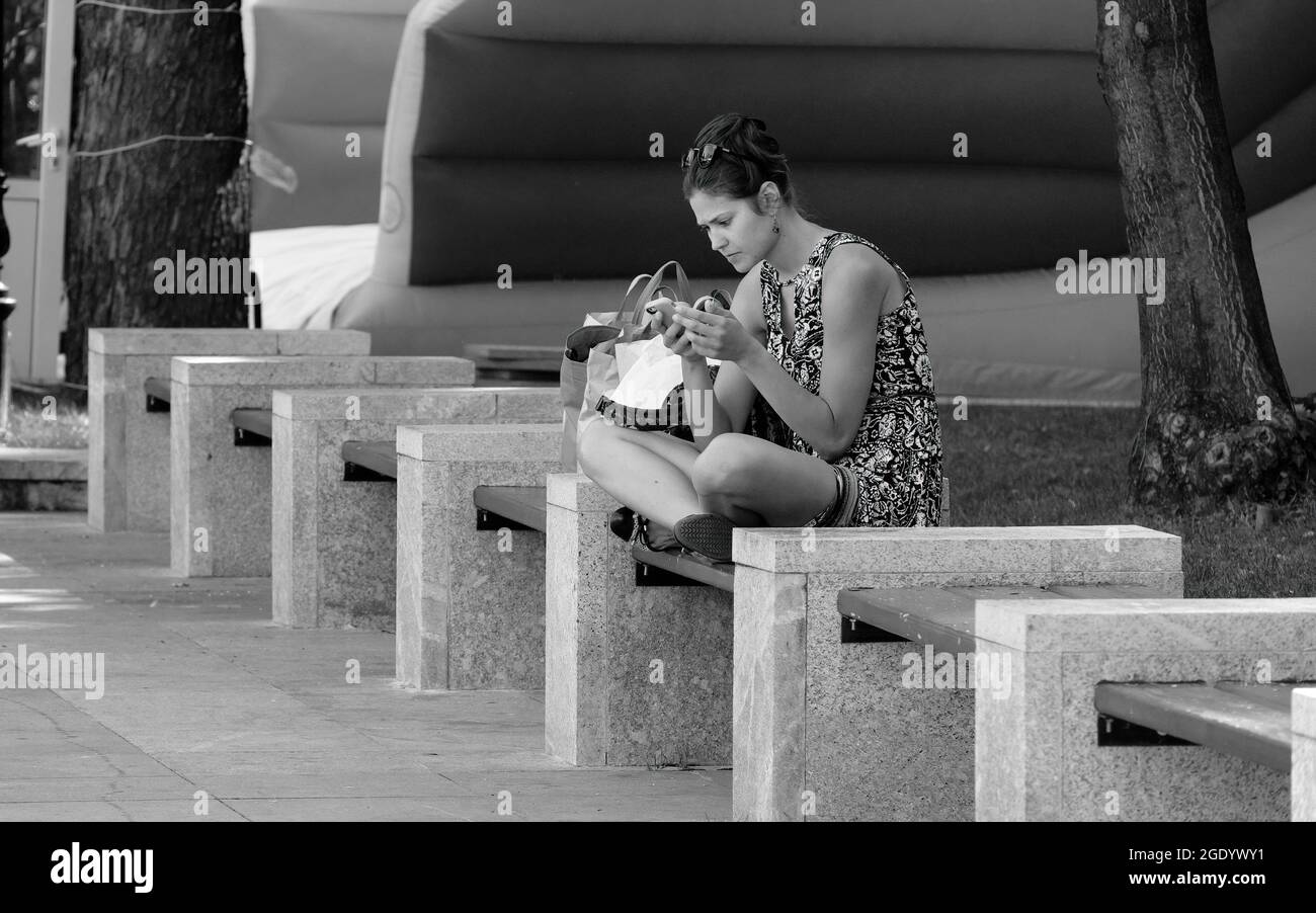 Giovane donna seduta sulla panchina e guardando il suo cellulare a Sofia, Bulgaria Foto Stock