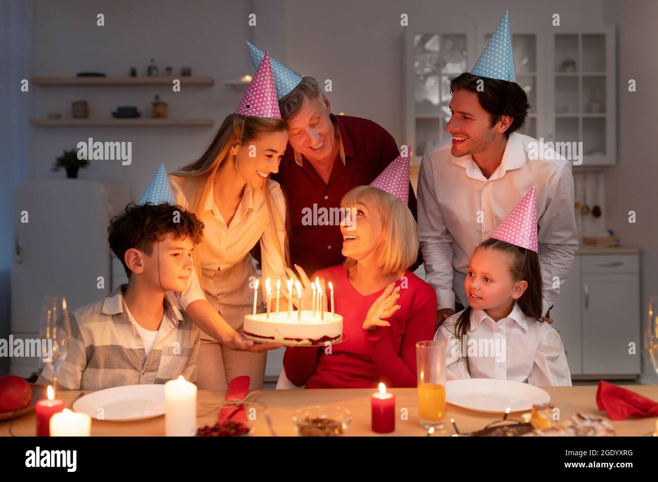 Felice estesa famiglia multigenerazione che ha festa di compleanno, dando donna anziana torta di b-day con candele a casa Foto Stock