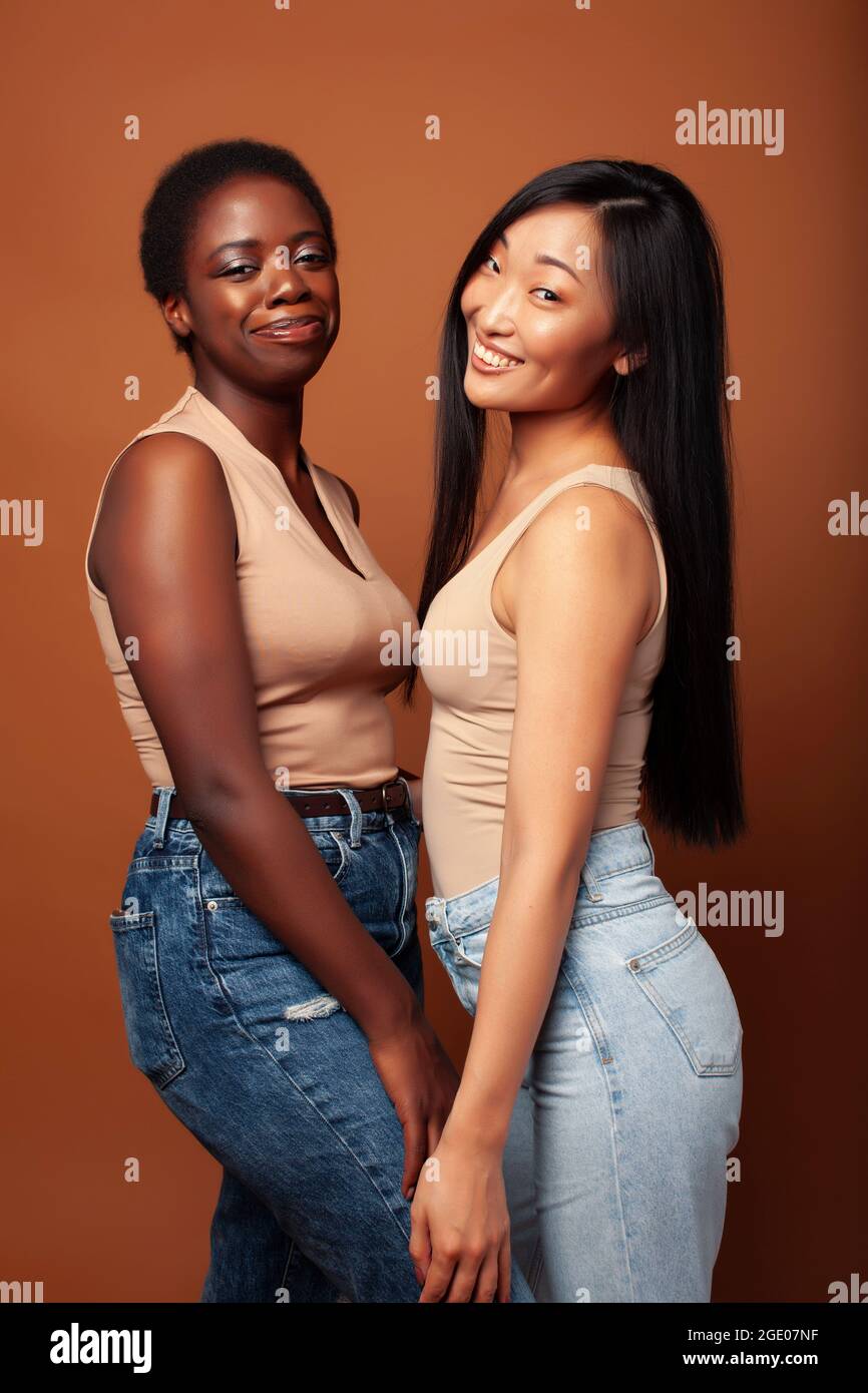 giovane bella asiatica, donna afro che si pone allegro insieme su sfondo marrone, stile di vita diversa nazionalità concetto di persone Foto Stock