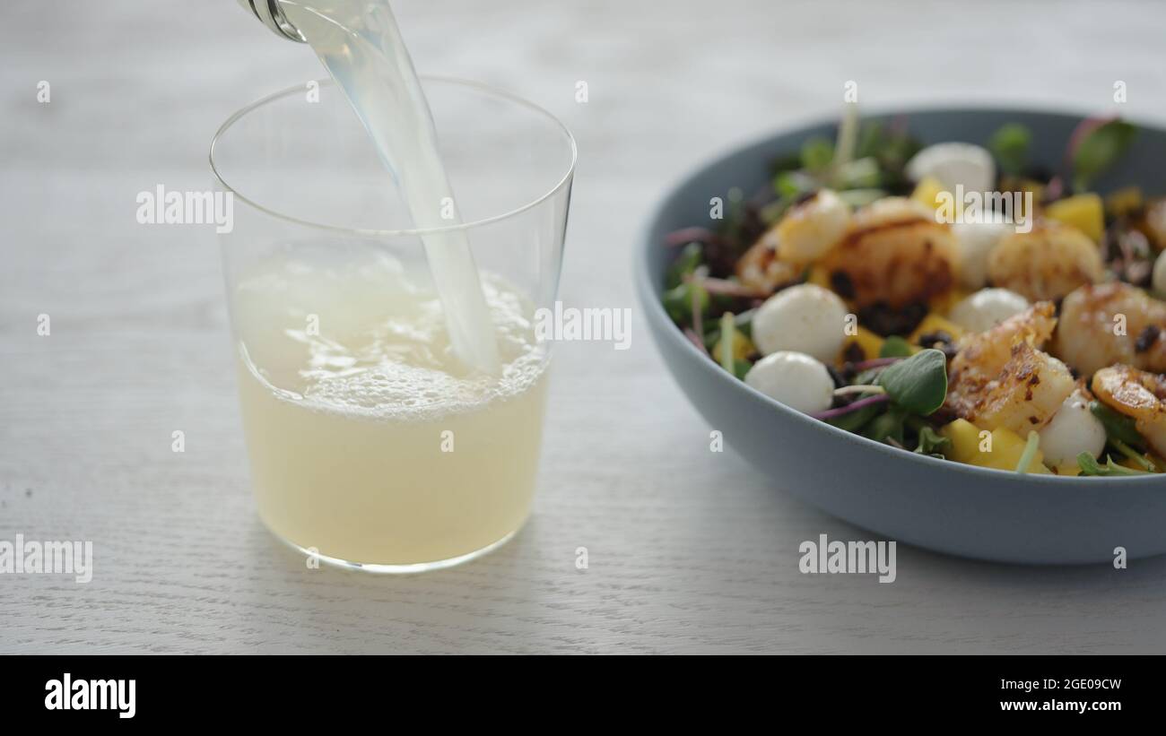 Man versare la limonata nel bicchiere accanto all'insalata con gamberetti, mango, mozzarella e micro green, foto ampia Foto Stock