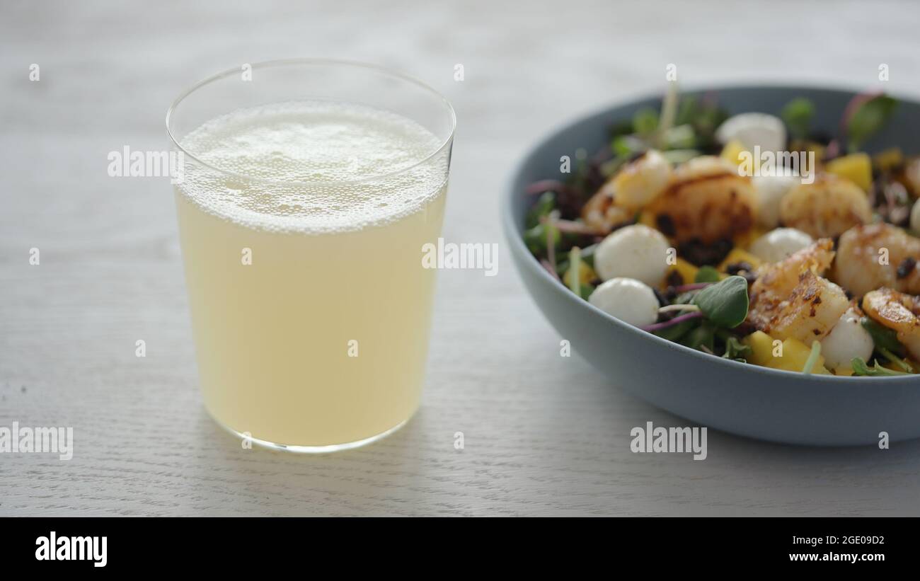 Limonata in bicchiere accanto all'insalata con gamberetti, mango, mozzarella e micro green foto ampia Foto Stock