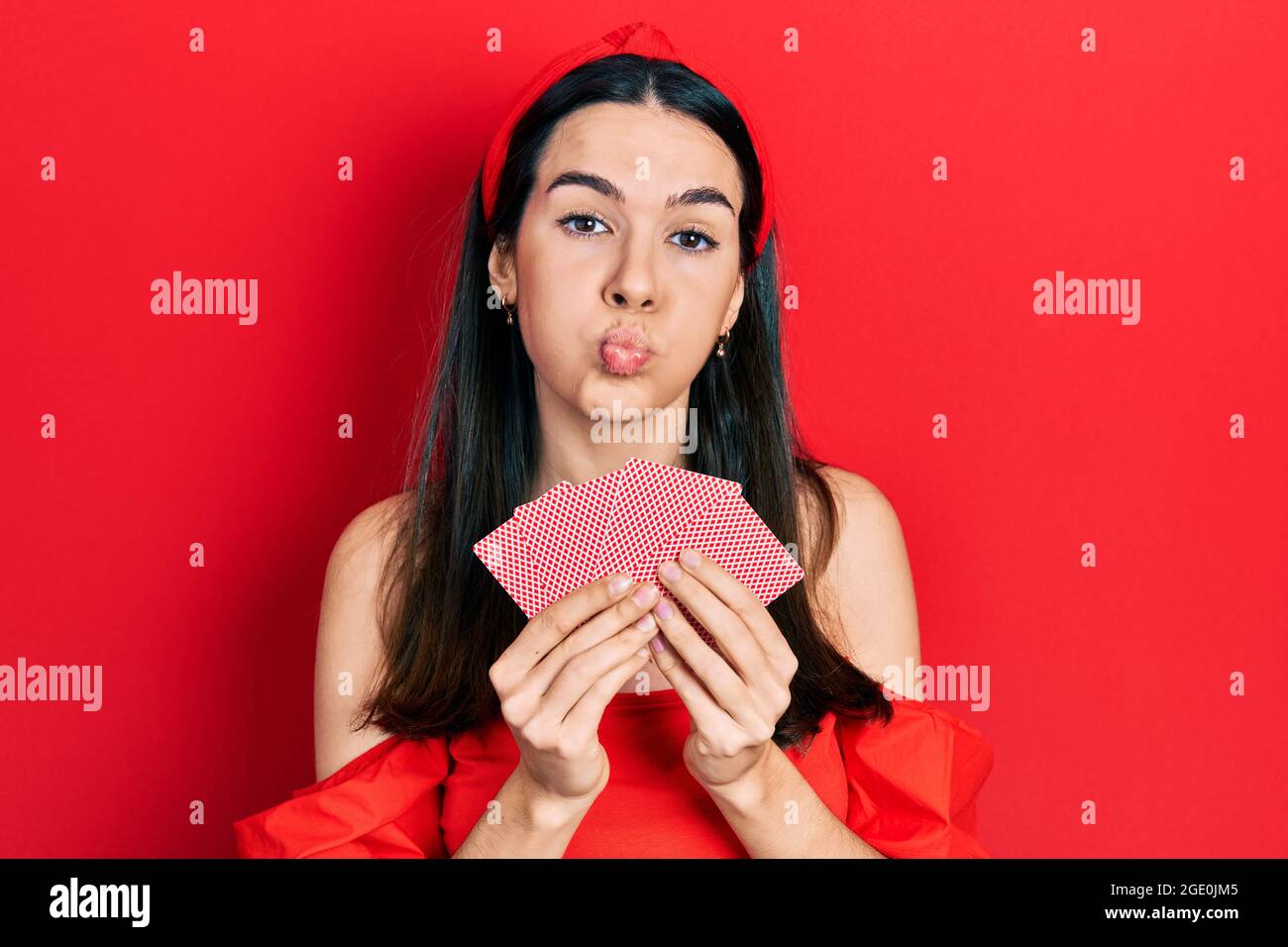 Giovane donna bruna che copre il viso con carte che soffocano le guance con il viso divertente. Bocca gonfia con aria, cattura aria. Foto Stock