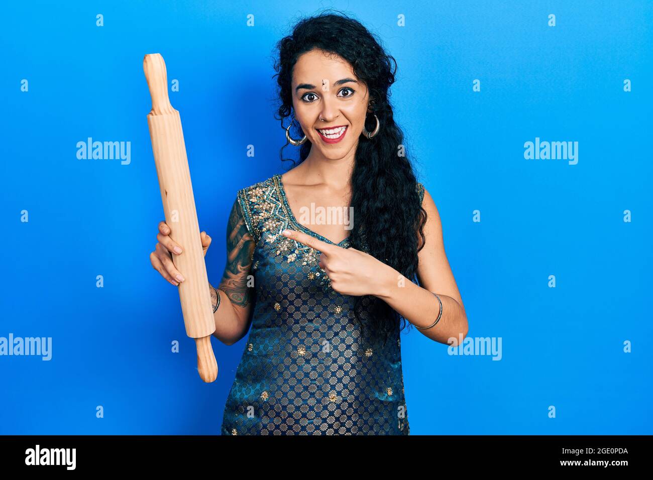 Giovane donna che indossa bindi e tradizionale abito kurta tenendo in mano il rullo impastatore sorridendo felice puntando con mano e dito Foto Stock