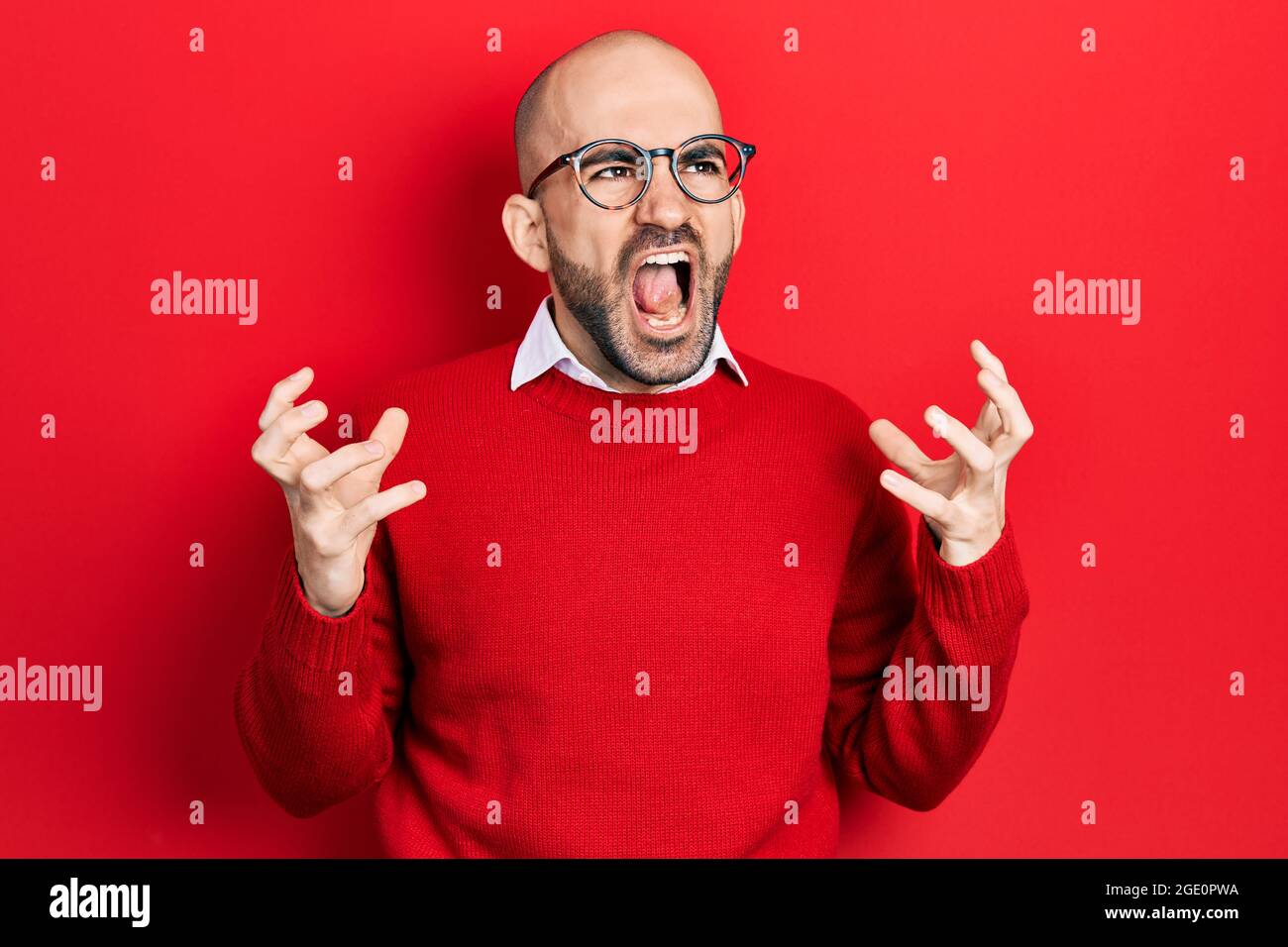 Giovane uomo calvo che indossa abiti casual e occhiali pazzo e pazzo gridando e urlando con espressione aggressiva e braccia sollevato. Concetto di frustrazione. Foto Stock
