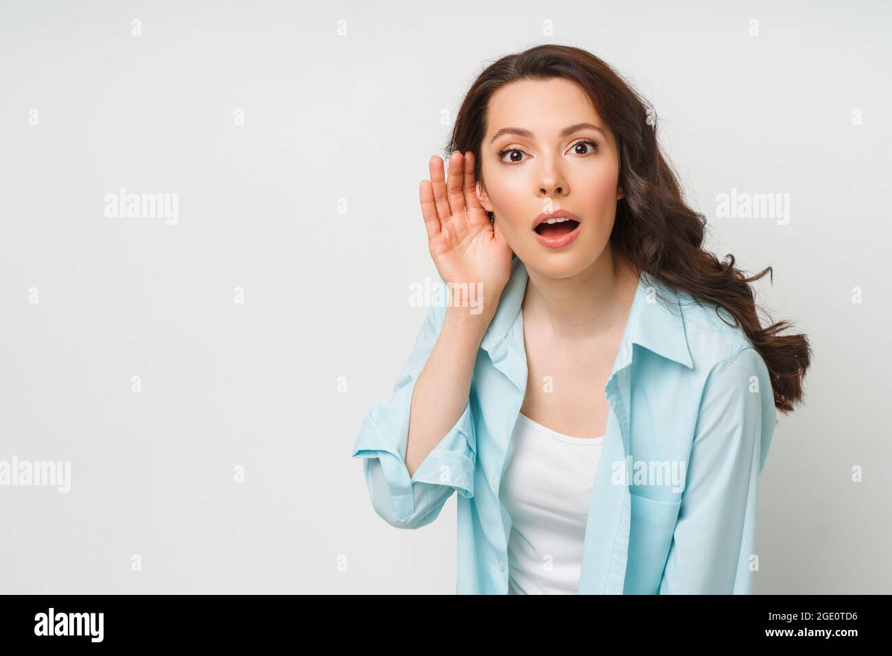 Una giovane donna si lancia sulla conversazione di qualcun altro con la mano all'orecchio. Il concetto di intercettazioni, spionaggio, pettegolezzi e la stampa gialla Foto Stock