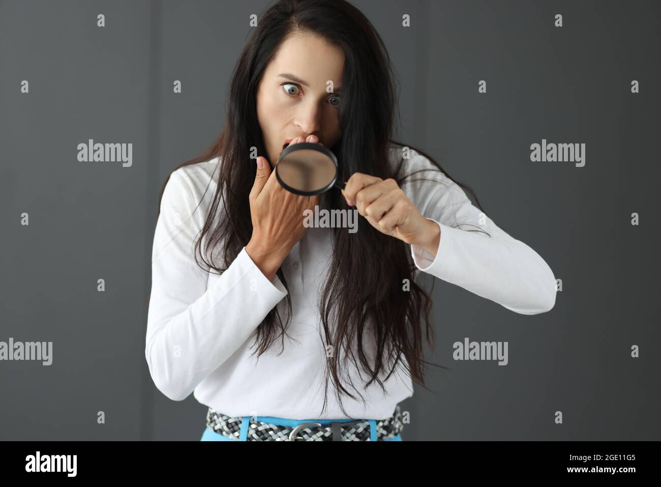 Donna sorpresa guardando attraverso la lente d'ingrandimento e coprendo la bocca con la mano Foto Stock