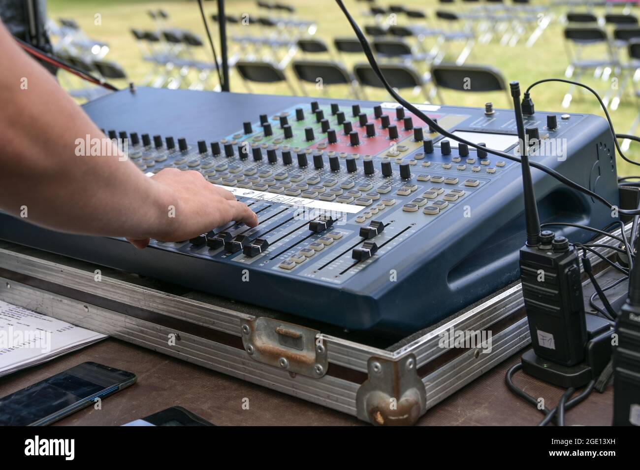 La mano del mixer audio preme i pulsanti su una console di mixaggio durante il controllo audio per un festival all'aperto, la messa a fuoco selezionata, la profondità di campo stretta Foto Stock